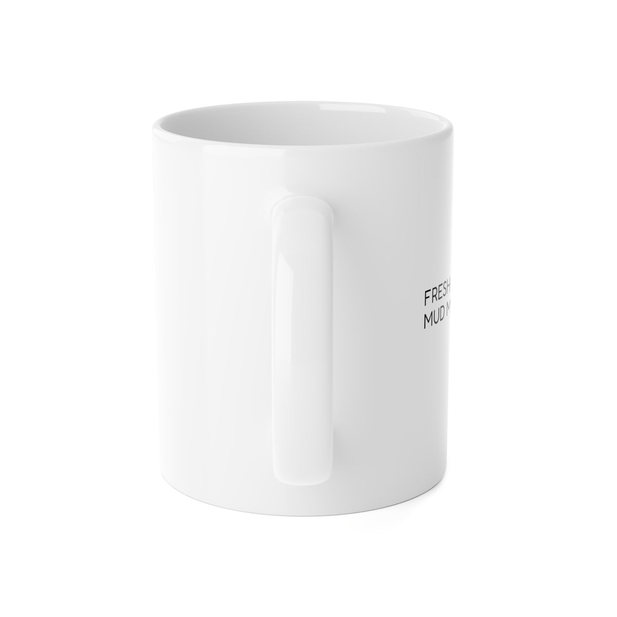 Rear-angle view of the white ceramic mug with part of the ‘Fresh Coat. Mud Magnet.’ design visible.